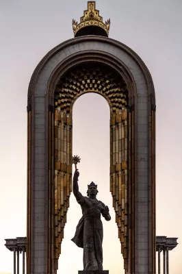 a statue with a torch in front of a large stone archway